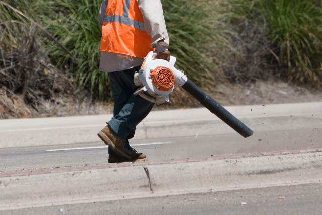 A worker holding blower and walking on road