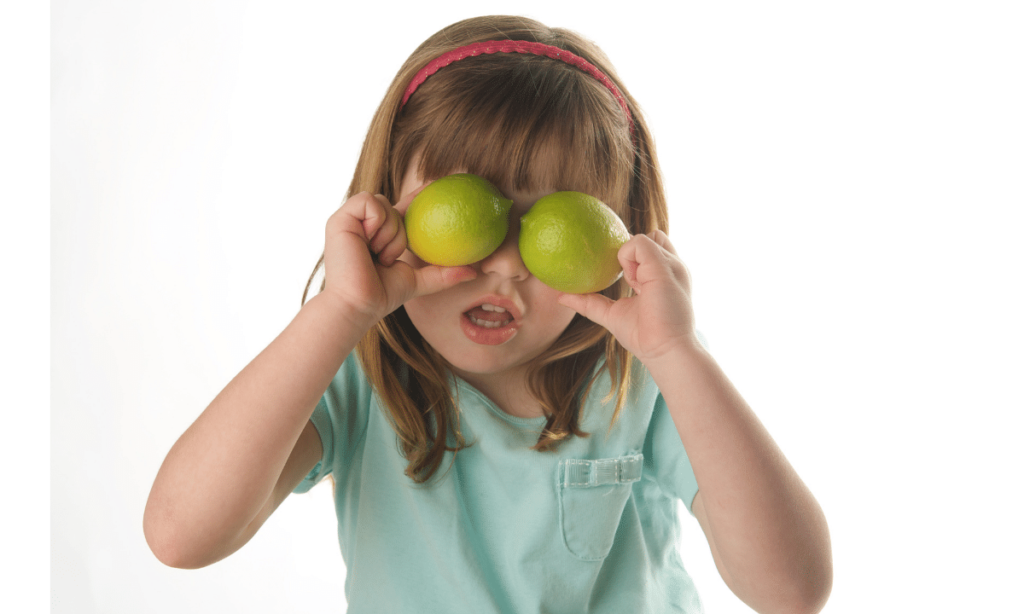 A little girl imitating green eyed mosnter by covering her eyes with lemons