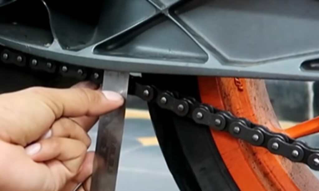 A guy measuring the motorcycle chain slack with a ruler