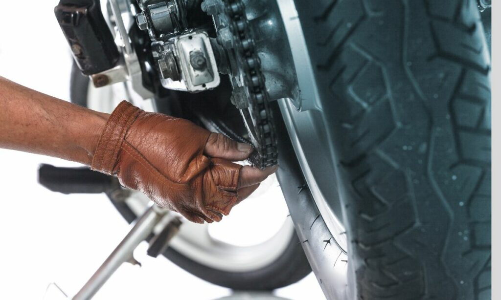 A guy with brown gloves on checking the motorcycle chain