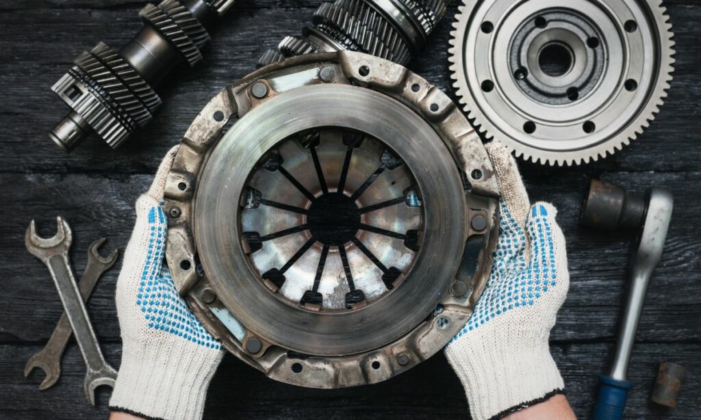 A guy holding a motorcycle clutch with gearbox in the background