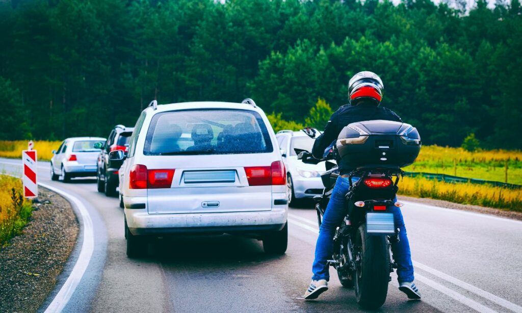 Motorcycle rider stopped behind cars on a traffic road